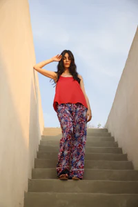 a woman in a red top and patterned pants standing on stairs